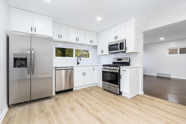 kitchen featuring appliances with stainless steel finishes, backsplash, sink, white cabinets, and light hardwood / wood-style floors