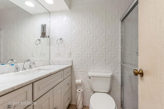 bathroom with vanity, toilet, a shower with door, and tile walls