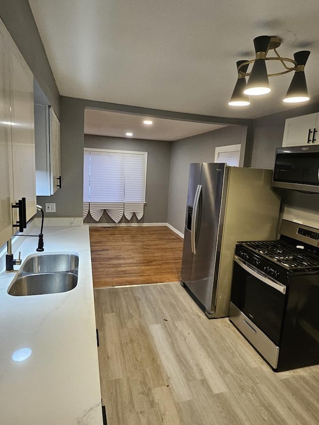 kitchen featuring white cabinetry, sink, pendant lighting, light hardwood / wood-style floors, and appliances with stainless steel finishes