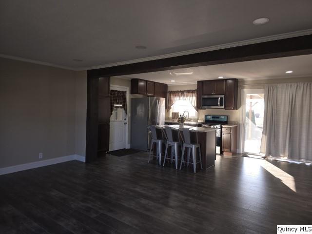 kitchen featuring a kitchen island, a breakfast bar, dark hardwood / wood-style flooring, ornamental molding, and stainless steel appliances