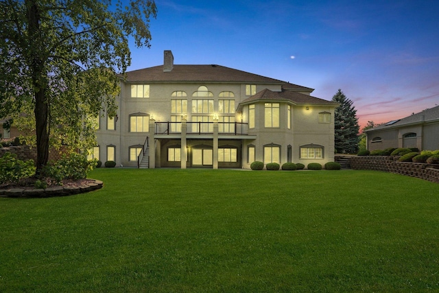 back house at dusk with a balcony and a lawn