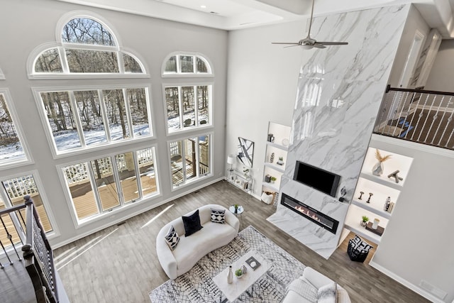 living room featuring a high ceiling, a premium fireplace, wood-type flooring, and ceiling fan