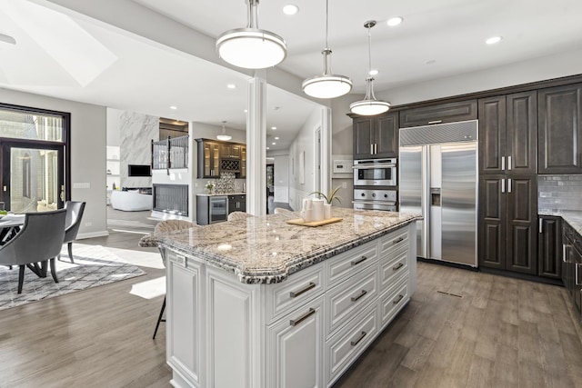 kitchen with decorative light fixtures, built in fridge, a kitchen island, beverage cooler, and white cabinets