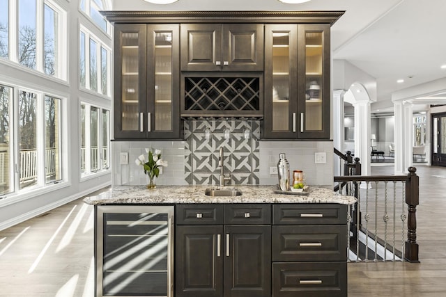 bar with decorative columns, light stone counters, beverage cooler, and light hardwood / wood-style floors