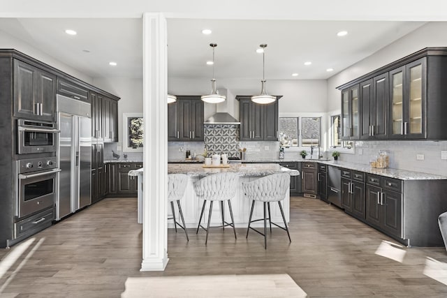 kitchen featuring appliances with stainless steel finishes, decorative light fixtures, a center island, light stone counters, and light hardwood / wood-style flooring