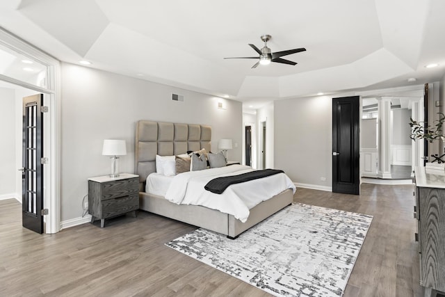 bedroom with ceiling fan, a tray ceiling, hardwood / wood-style floors, and decorative columns