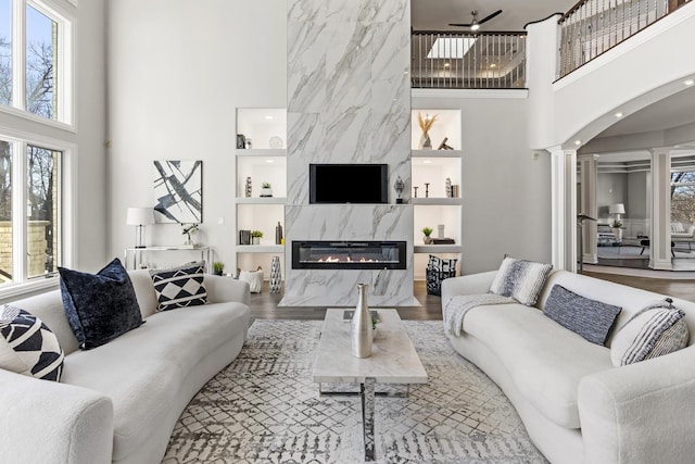 living room with a premium fireplace, hardwood / wood-style floors, a high ceiling, built in shelves, and ornate columns