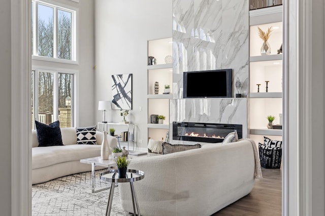 living room featuring hardwood / wood-style floors, built in features, a premium fireplace, and a high ceiling