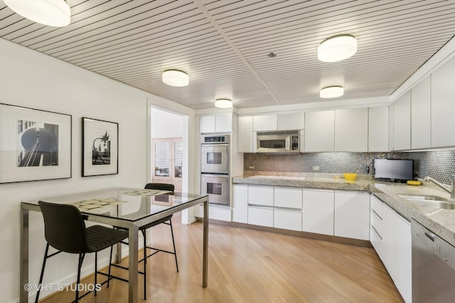 kitchen with sink, appliances with stainless steel finishes, tasteful backsplash, white cabinets, and light wood-type flooring