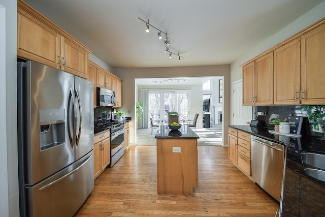 kitchen with decorative backsplash, dark stone countertops, a kitchen island, light hardwood / wood-style flooring, and stainless steel appliances