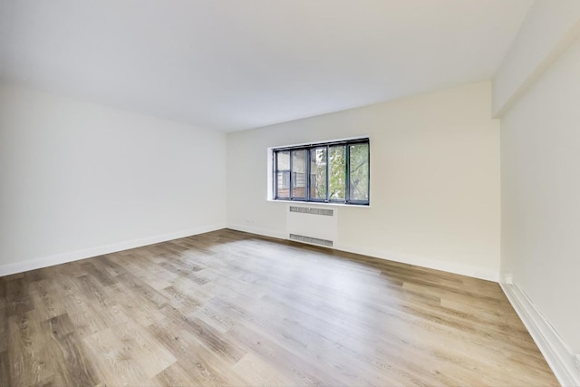 empty room with light hardwood / wood-style floors and radiator heating unit