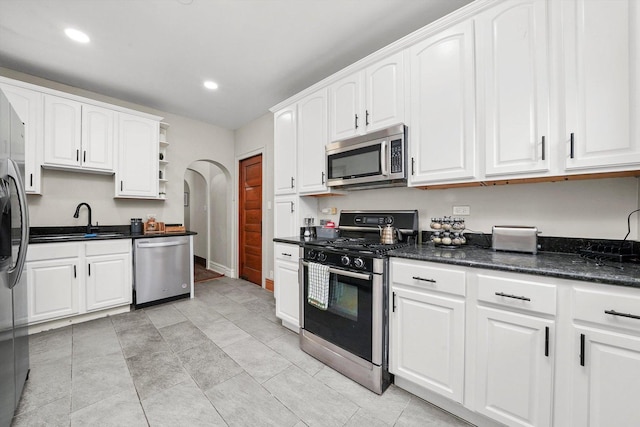 kitchen with dark stone counters, white cabinetry, sink, and stainless steel appliances