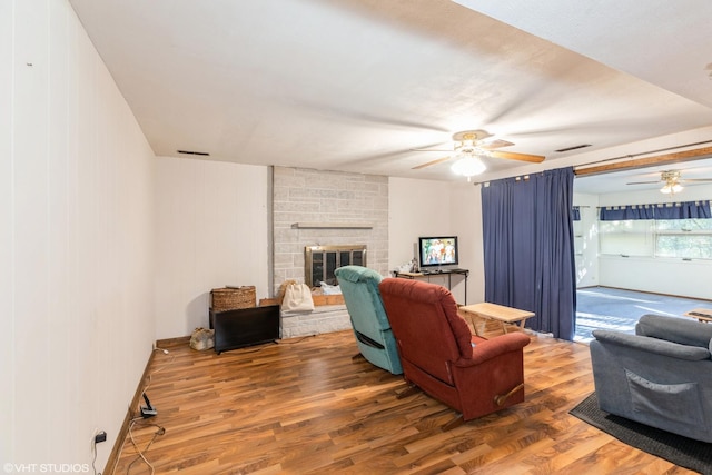 living room with wood-type flooring, a stone fireplace, and ceiling fan