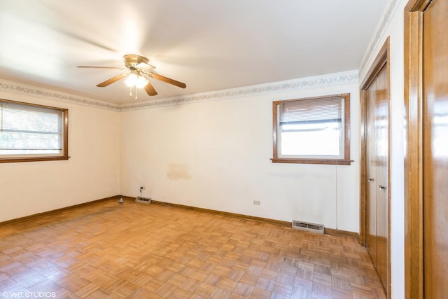 empty room with a wealth of natural light, light parquet flooring, and ceiling fan