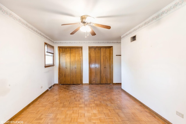 unfurnished bedroom featuring light parquet floors, ceiling fan, multiple closets, and crown molding