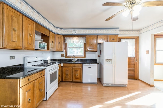 kitchen with dark stone counters, white appliances, ceiling fan, sink, and light hardwood / wood-style floors