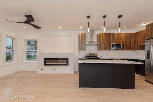 kitchen featuring a center island, decorative light fixtures, wall chimney range hood, appliances with stainless steel finishes, and ceiling fan