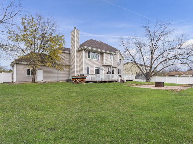 rear view of property with a lawn, a wooden deck, and a fire pit