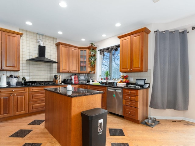 kitchen with a center island, backsplash, wall chimney range hood, stainless steel dishwasher, and dark stone countertops