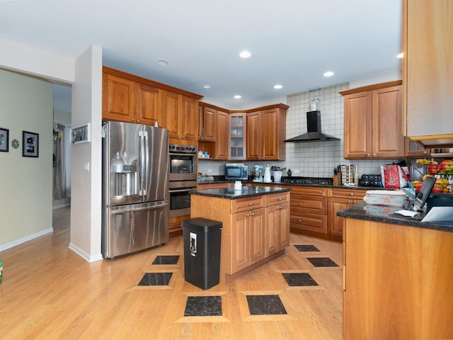 kitchen with wall chimney exhaust hood, dark stone countertops, appliances with stainless steel finishes, tasteful backsplash, and a kitchen island