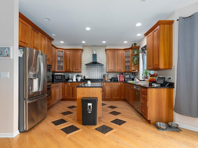 kitchen featuring appliances with stainless steel finishes, tasteful backsplash, wall chimney exhaust hood, light hardwood / wood-style floors, and a kitchen island