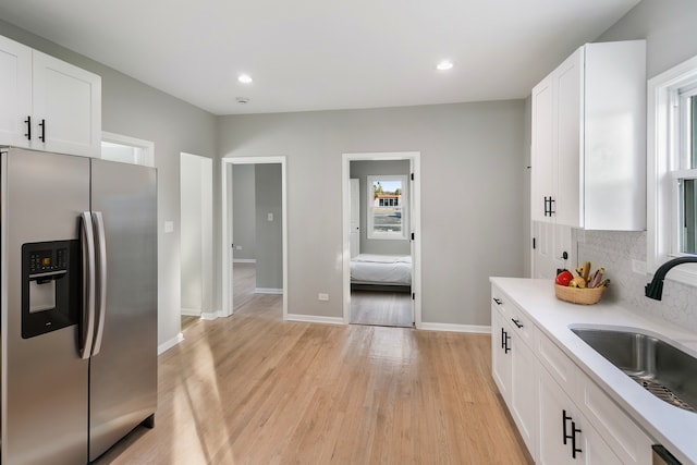 kitchen with a wealth of natural light, sink, stainless steel fridge with ice dispenser, light hardwood / wood-style flooring, and white cabinets