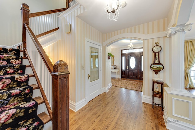 foyer featuring arched walkways, stairway, wallpapered walls, light wood finished floors, and an inviting chandelier