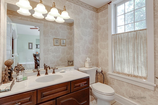 bathroom with toilet, wallpapered walls, baseboards, and vanity