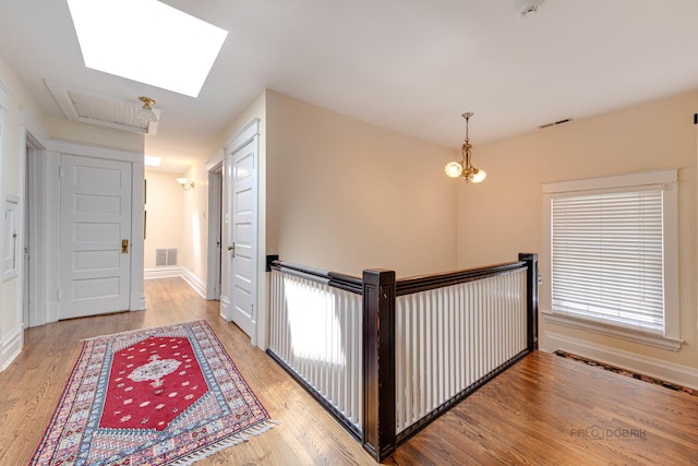 hallway with light wood-type flooring, a skylight, baseboards, and visible vents