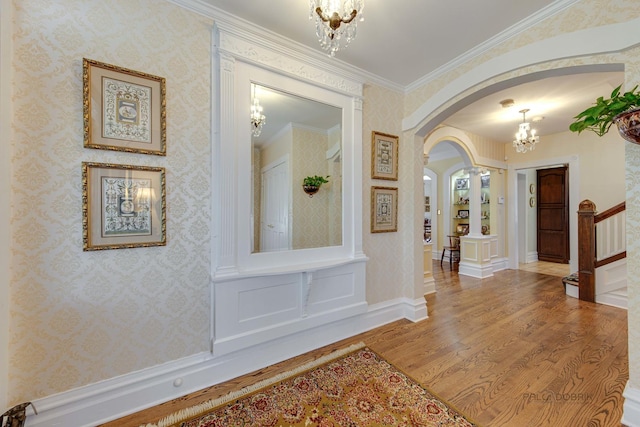 hall with wallpapered walls, arched walkways, wood finished floors, crown molding, and a notable chandelier