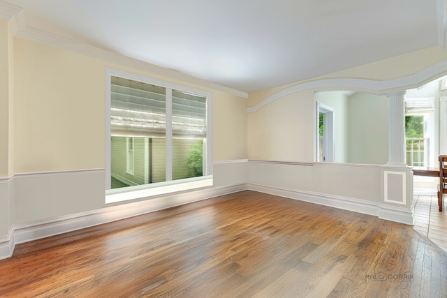 spare room featuring decorative columns, crown molding, and wood finished floors