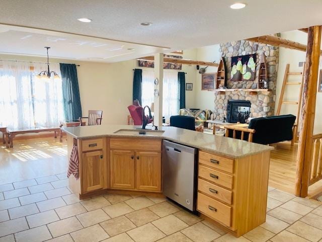 kitchen with sink, stainless steel dishwasher, an island with sink, decorative light fixtures, and a fireplace