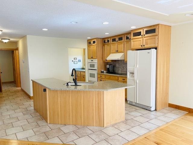 kitchen featuring sink, backsplash, white appliances, a kitchen island with sink, and light tile patterned floors