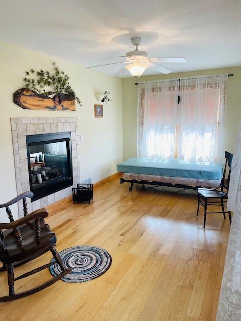 living room featuring hardwood / wood-style flooring, ceiling fan, and a tiled fireplace