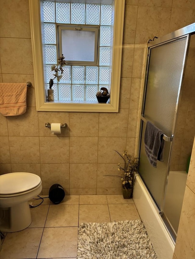 bathroom with tile patterned floors, toilet, enclosed tub / shower combo, and tile walls