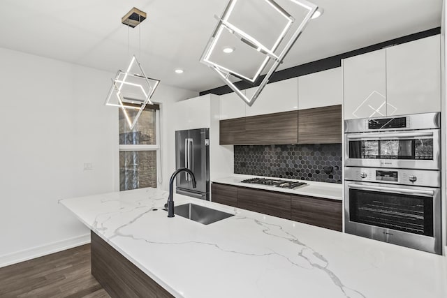 kitchen with sink, light stone countertops, tasteful backsplash, decorative light fixtures, and stainless steel appliances