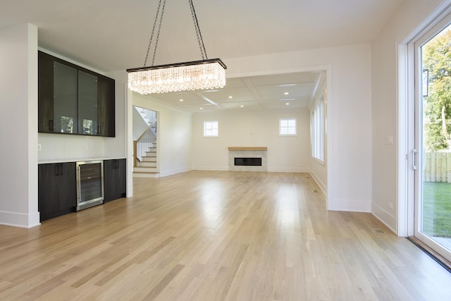 unfurnished living room featuring coffered ceiling, an inviting chandelier, beam ceiling, light hardwood / wood-style floors, and beverage cooler