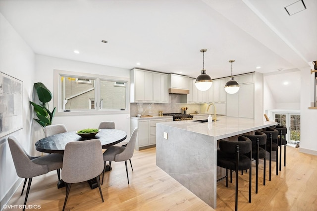 kitchen with white cabinetry, sink, hanging light fixtures, light stone counters, and custom range hood