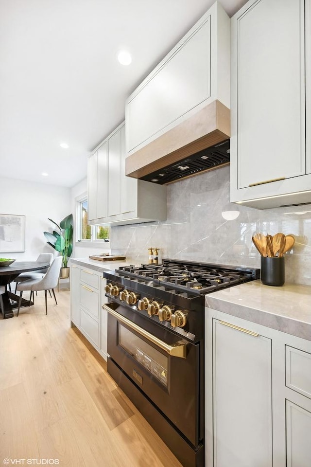 kitchen featuring decorative backsplash, light wood-type flooring, white cabinetry, and high end black range