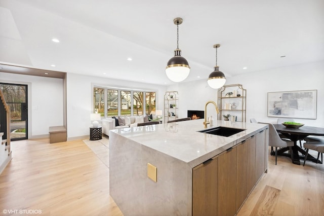 kitchen with light stone countertops, a spacious island, sink, decorative light fixtures, and light hardwood / wood-style flooring