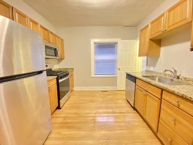 kitchen with appliances with stainless steel finishes, light hardwood / wood-style flooring, light stone countertops, and sink