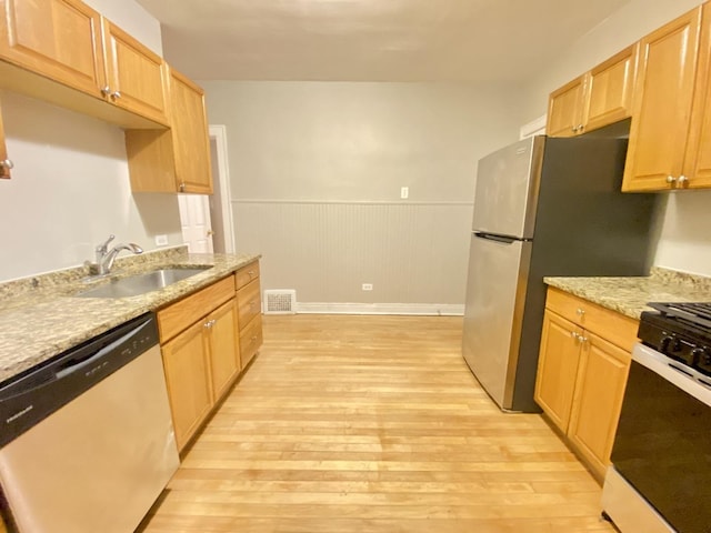 kitchen featuring sink, light hardwood / wood-style floors, light stone counters, and appliances with stainless steel finishes