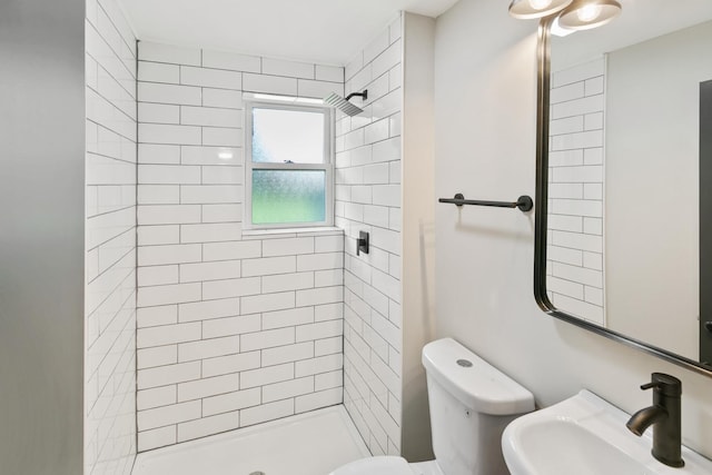 bathroom featuring tiled shower, toilet, and sink