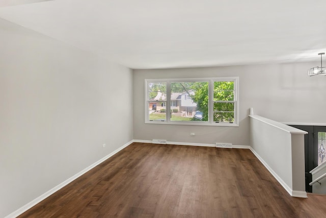 empty room with dark hardwood / wood-style flooring and a notable chandelier