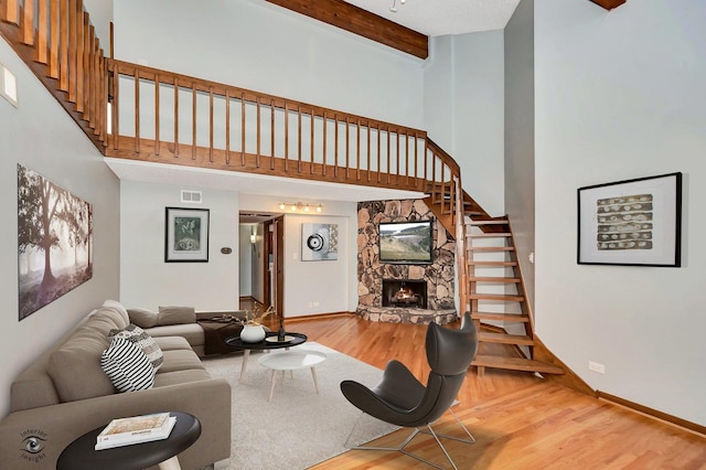 living room with a fireplace, hardwood / wood-style floors, beamed ceiling, and a towering ceiling