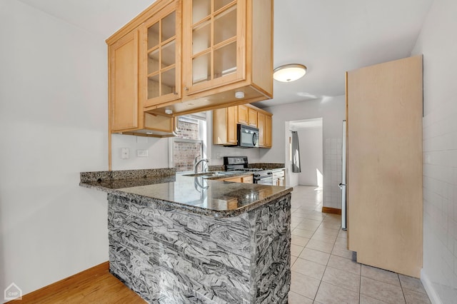 kitchen with dark stone counters, sink, light tile patterned floors, gas stove, and kitchen peninsula