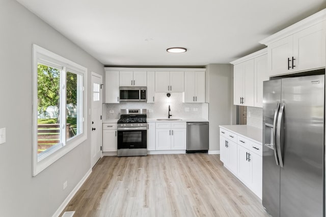 kitchen with white cabinets, sink, light wood-type flooring, appliances with stainless steel finishes, and tasteful backsplash