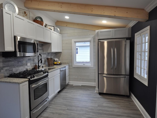 kitchen with white cabinetry, stainless steel appliances, lofted ceiling with beams, light stone counters, and sink