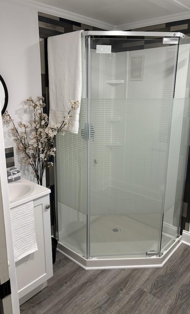 bathroom with a shower with shower door, wood-type flooring, vanity, and ornamental molding