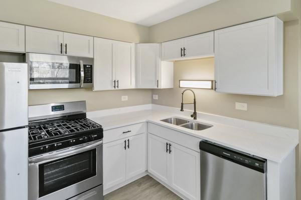 kitchen featuring white cabinetry, sink, light wood-type flooring, and appliances with stainless steel finishes